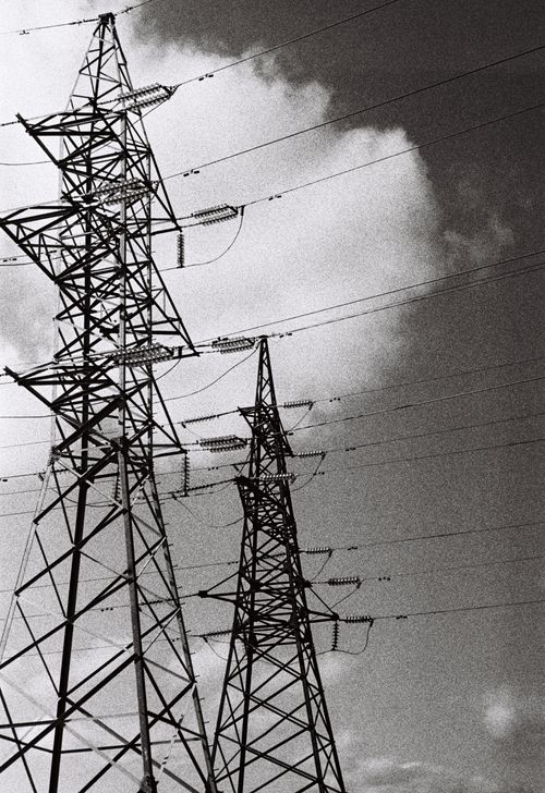 Free Monochrome photograph of towering power lines set against a dramatic cloudy sky. Stock Photo