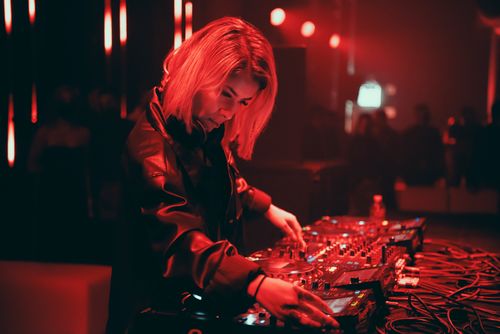Free A dynamic female DJ performs live at a bustling nightclub in red ambient lighting. Stock Photo