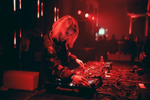 Free A female DJ mixing tracks in an atmospheric red-lit nightclub setting, engaging the crowd with electronic music. Stock Photo