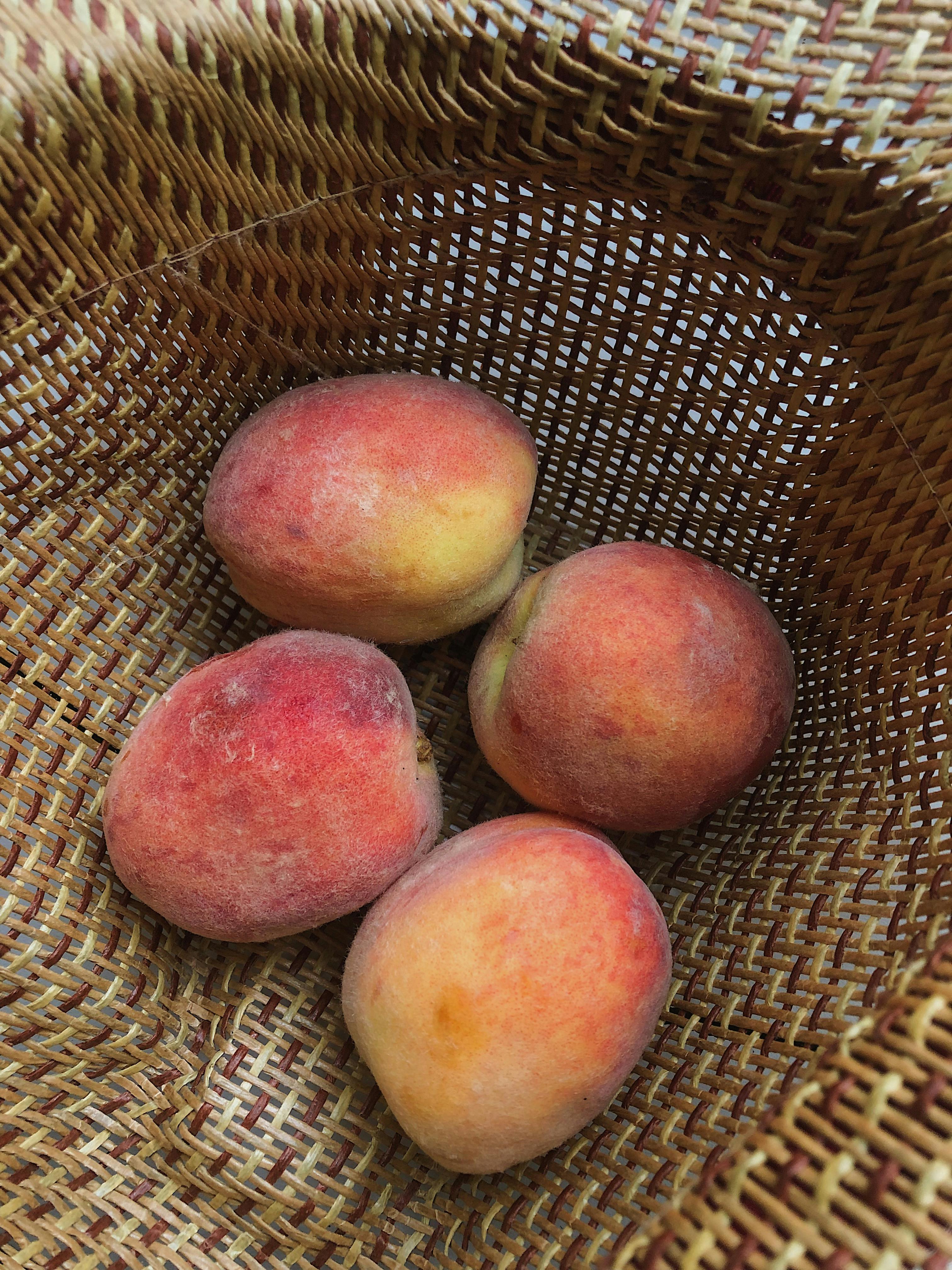 Close-up of ripe peaches in a woven basket, showcasing their freshness and natural texture.