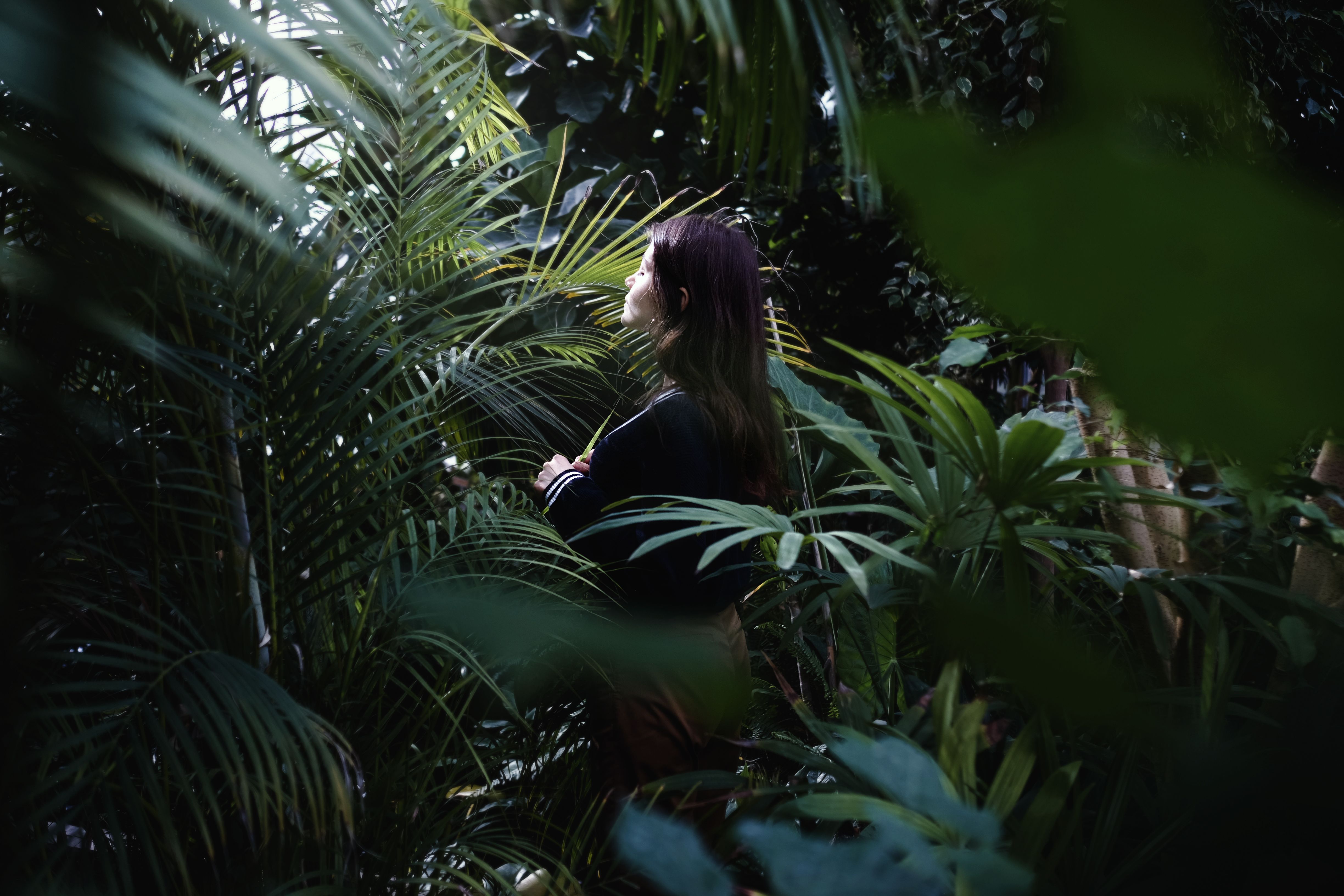 Woman in Black Jacket Standing Beside Green Plants · Free Stock Photo