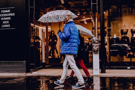 Two people walk with umbrellas on a rainy city street, wearing stylish winter attire.
