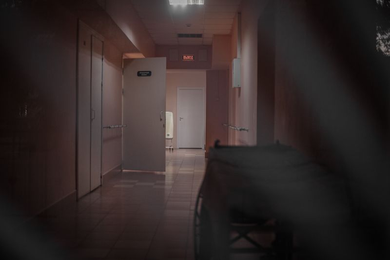 A deserted hospital corridor with open doors and dim lighting, enhancing a mysterious ambiance.