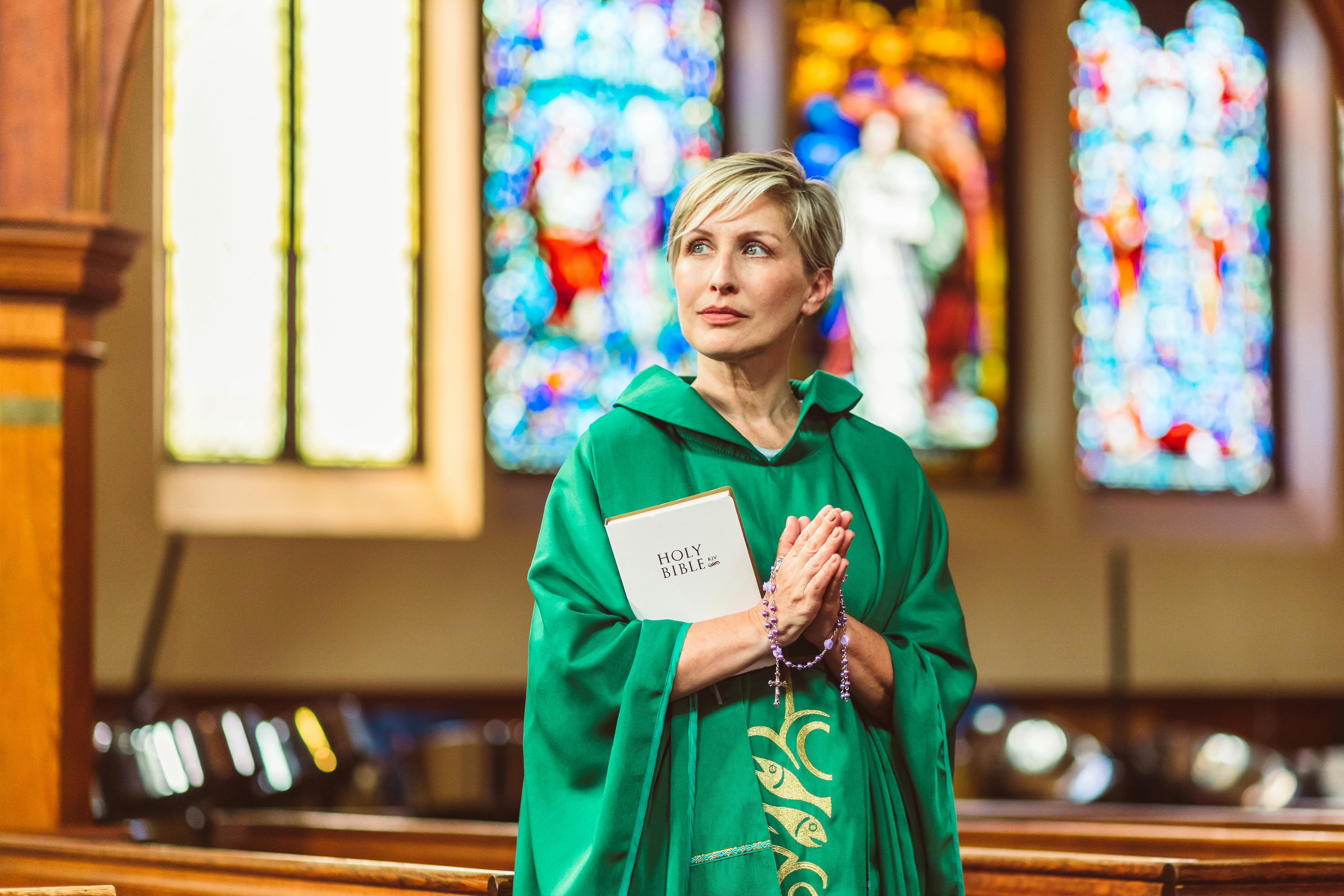 woman in green chasuble holding a bible and rosary with praying hands