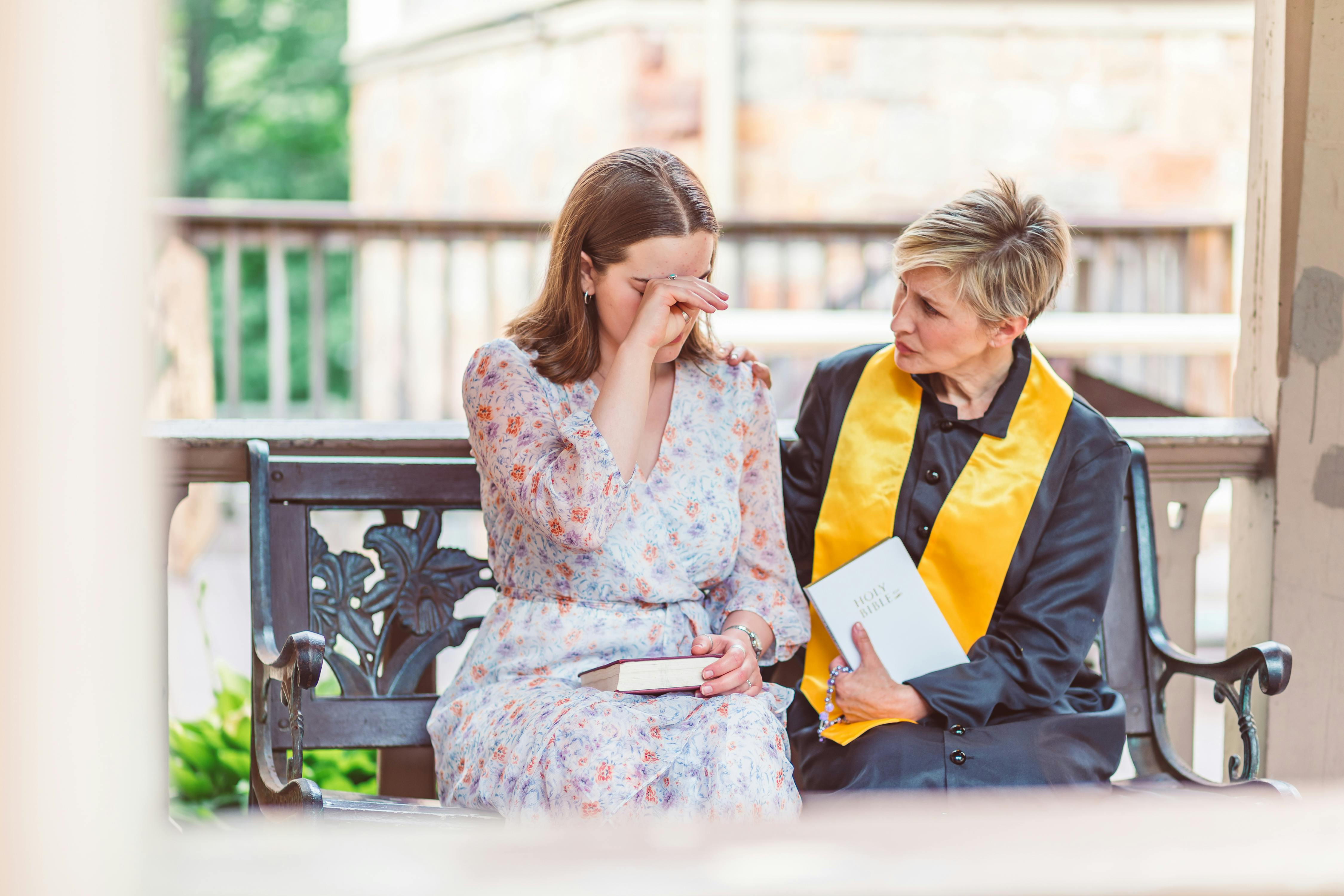 Free Woman in White Floral Dress Sitting on Bench with a Priest Stock Photo