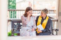 Woman in White Floral Dress Sitting on Bench with a Priest