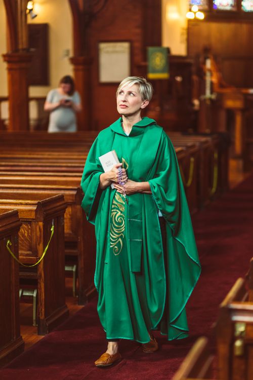 Free A woman in green robes holding a Bible standing in a church aisle, embracing faith and reflection. Stock Photo