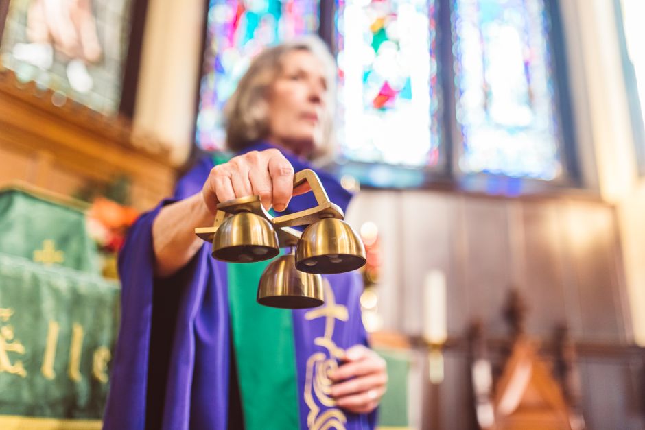 A priest holding altar bells during a religious ceremony in a church.