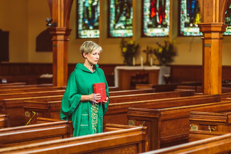 Woman In Green Chasuble Walking On Church Aisle Holding A Bible