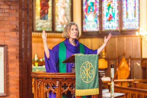 Eldelry Woman in Cassock Standing Behind Podium 