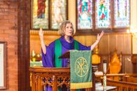 Eldelry Woman in Cassock Standing Behind Podium