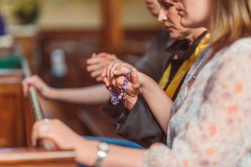 Free Group of people praying with rosary beads in a church, conveying faith and spirituality. Stock Photo