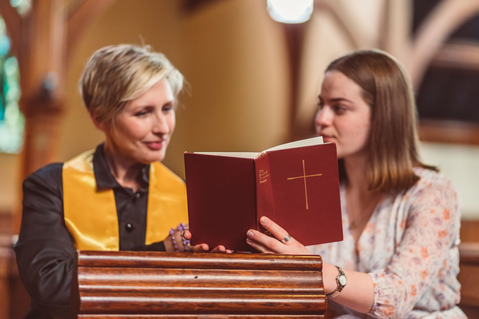 Two women reading the Bible together inside a church, focusing on religious study.