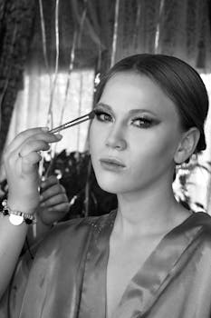 Black and white portrait of a woman getting eye makeup applied during a photoshoot.