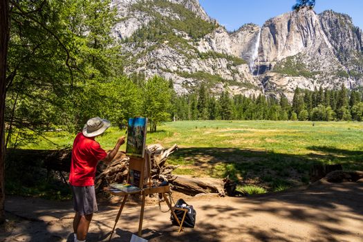 A painter captures the serene beauty of Yosemite Valley with waterfalls and lush greenery under clear skies.