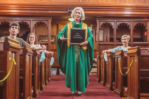 Free A church service where mask policies have changed, featuring a priest with a sign. Stock Photo