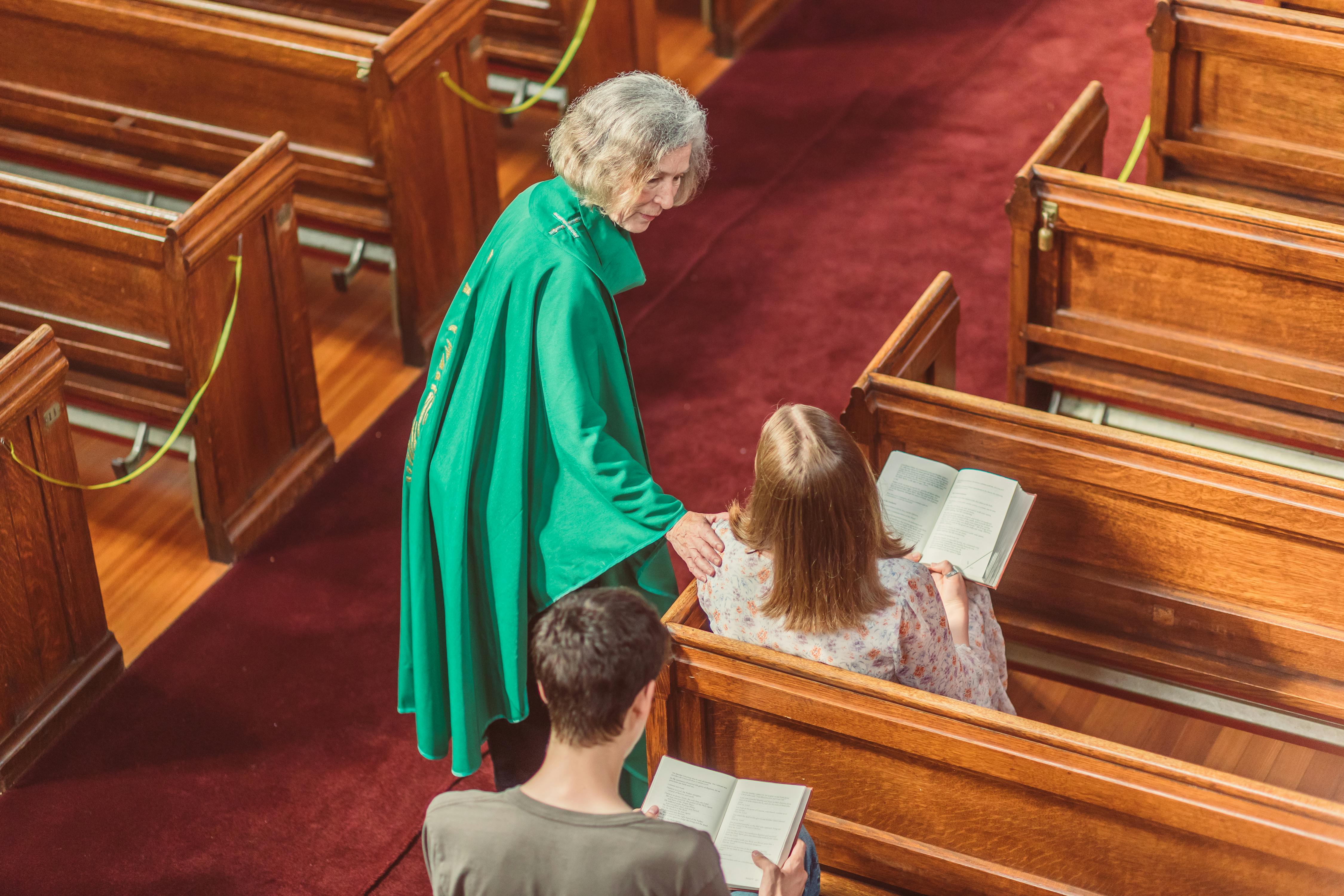 elderly woman in green cassock looking at a parishioner