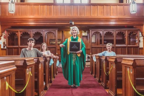 Free A group in a church pew with a woman holding a 'No Masks Required' sign, indicating a change in safety measures. Stock Photo