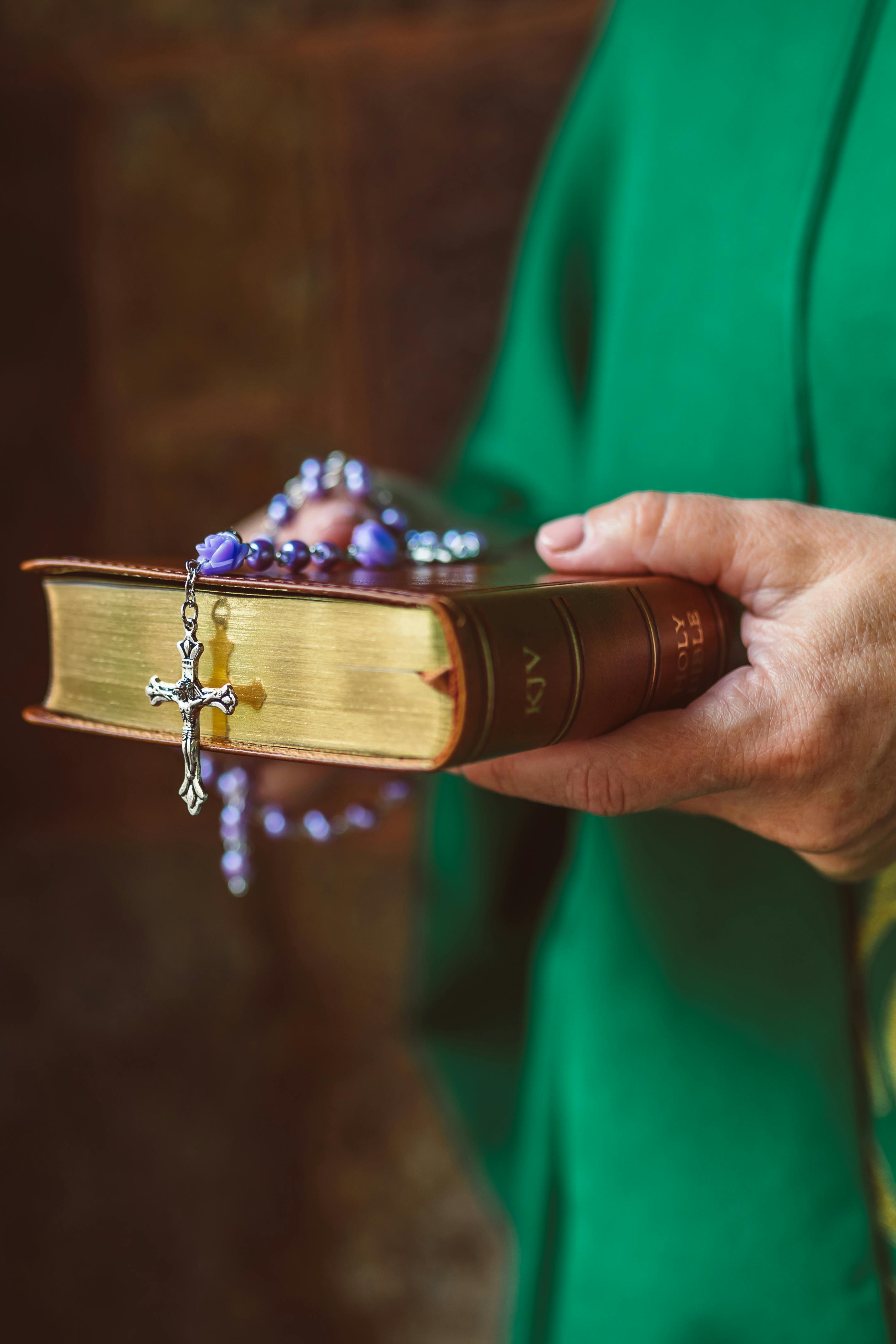 person holding bible with rosary on top