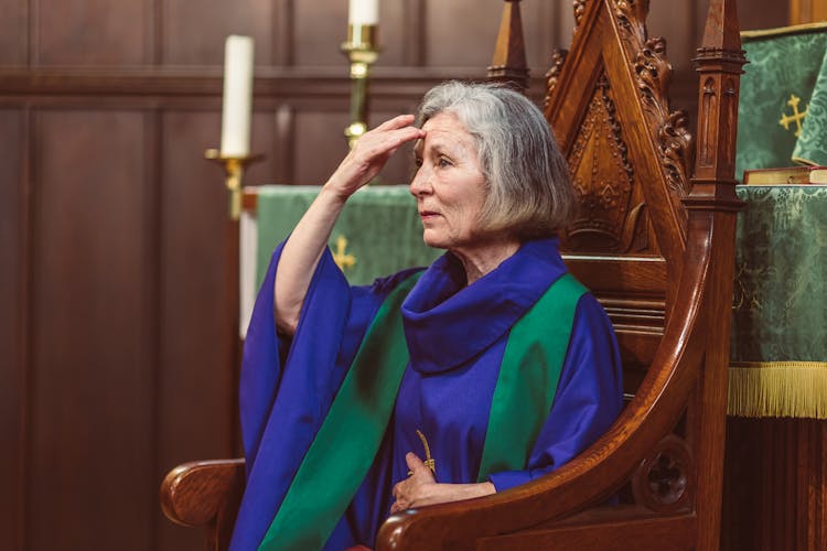 Female Priest Sitting On A Cathedra Doing The Sign Of The Cross