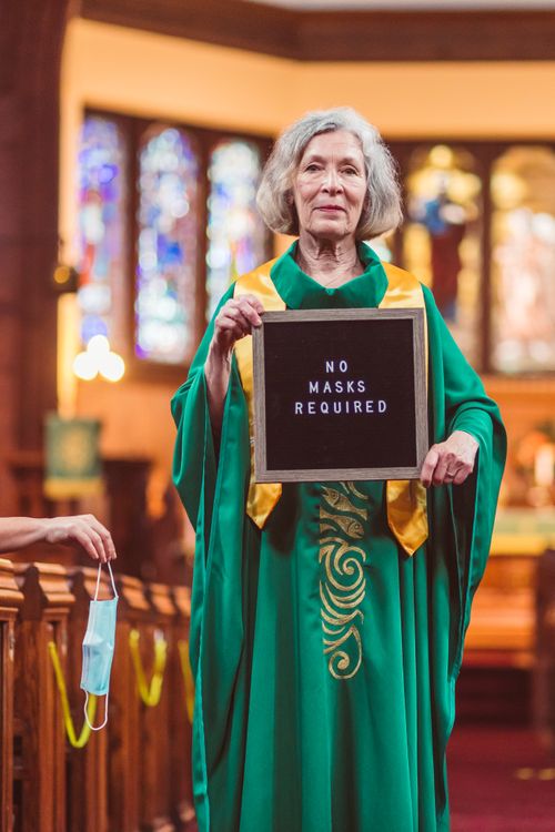 Free Elderly woman in church holding no masks required sign, symbolizing end of restrictions. Stock Photo