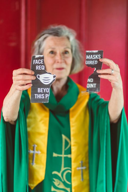 Free Senior female priest tearing a face mask requirement sign in church setting. Stock Photo