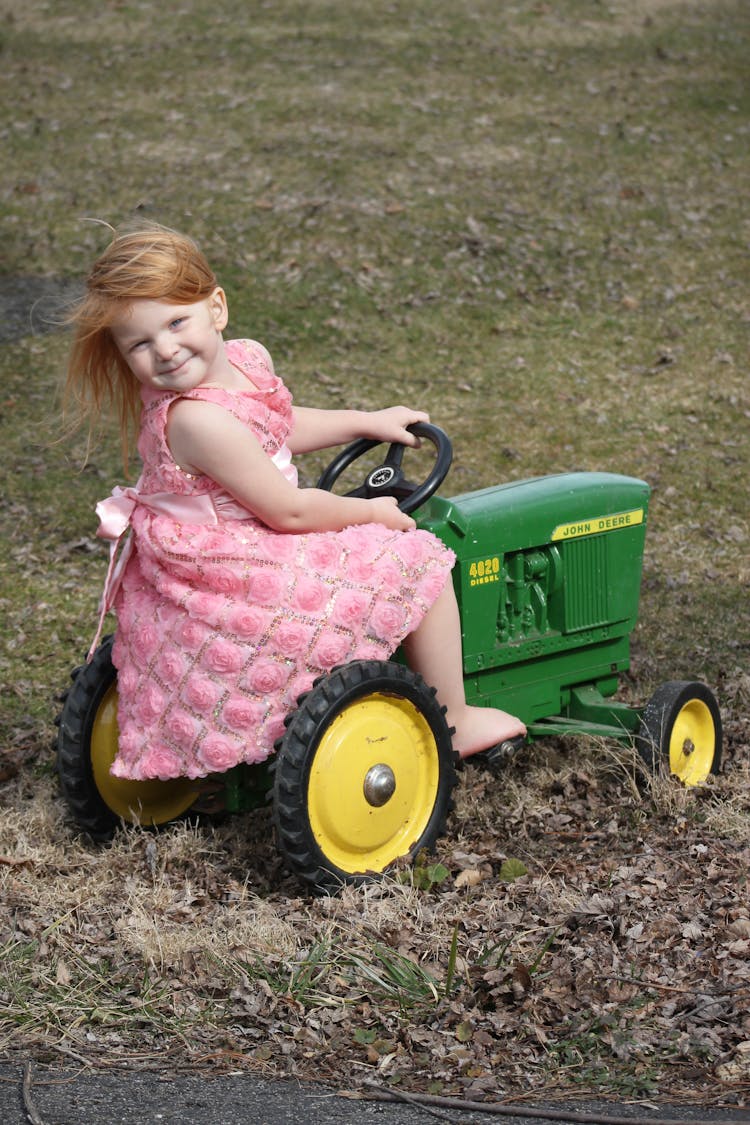 Cute Girl In Pink Dress Using A Tractor