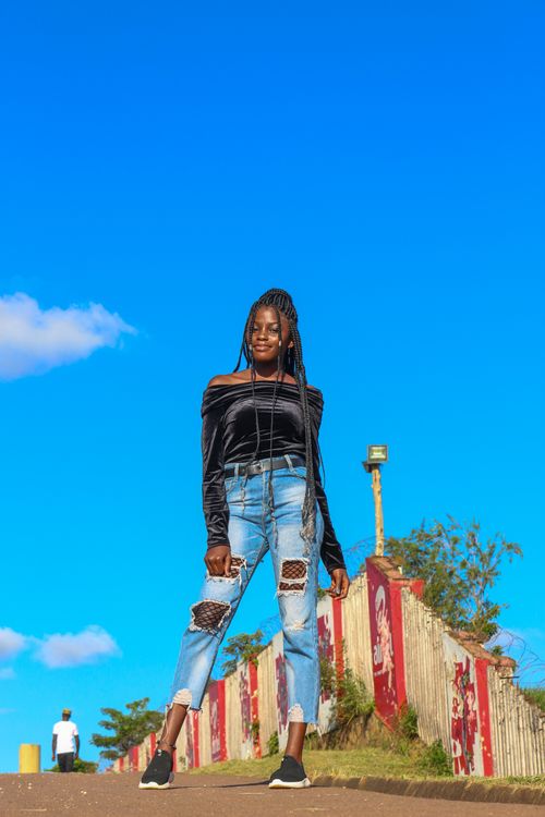 Free Stylish woman in black top and jeans against a vibrant blue sky and urban backdrop. Stock Photo
