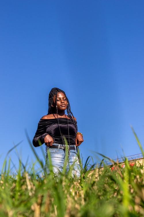 Free A woman posing confidently in a grassy field with a bright blue sky backdrop in Kampala, Uganda. Stock Photo
