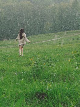 A woman joyfully runs through a green meadow in the rain, embracing nature.