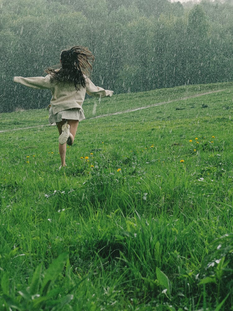 A Person Running In A Grass Field While Raining