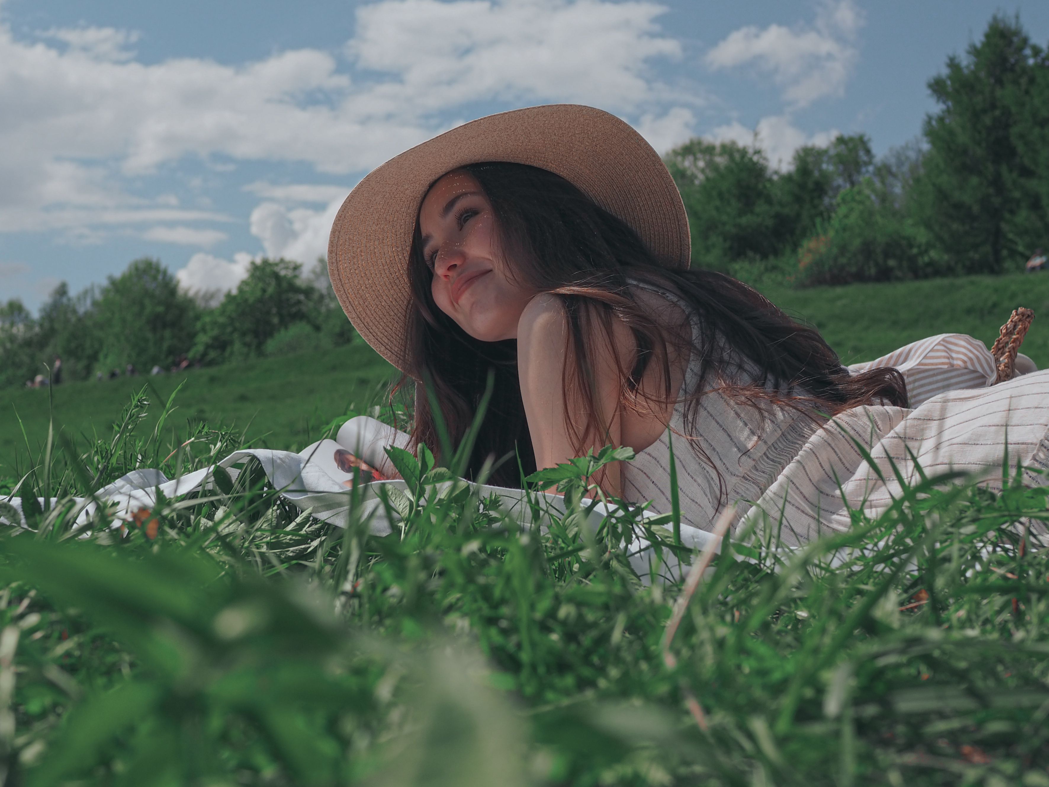 A serene image of a woman in a sun hat lounging on grass under a blue sky.