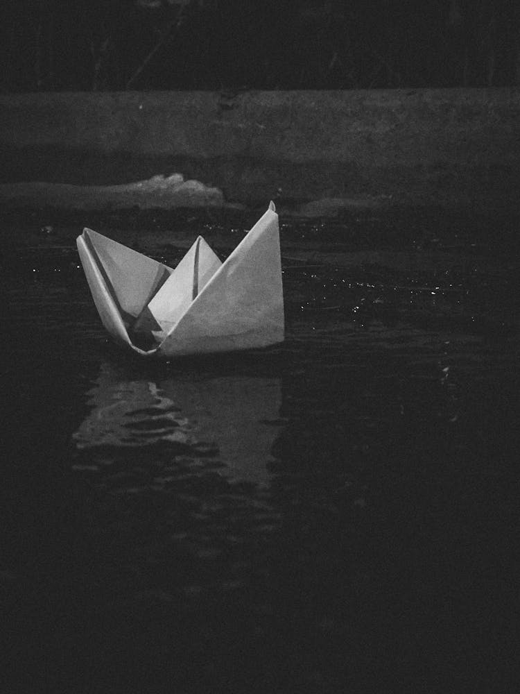 Grayscale Photo Of An Origami Boat On Water