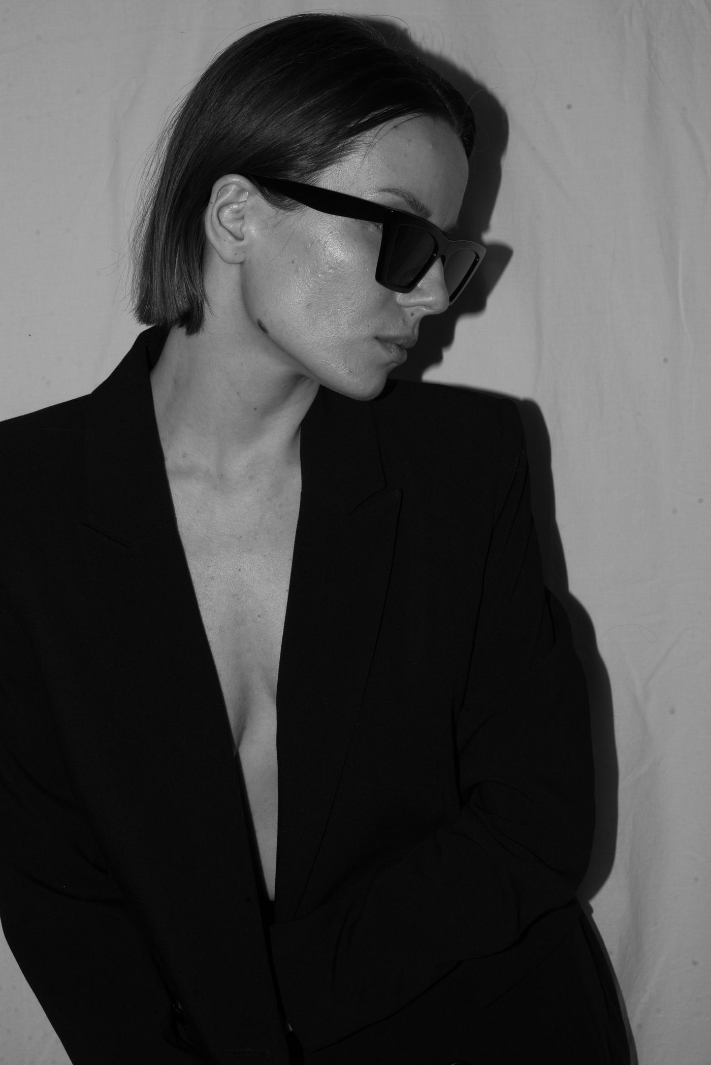A woman in a black suit jacket wearing black sunglasses — sharp, editorial styling