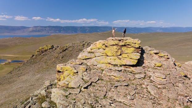 Two adventurers standing atop a rocky formation overlooking Lake Baikal in Siberia's summer landscape.