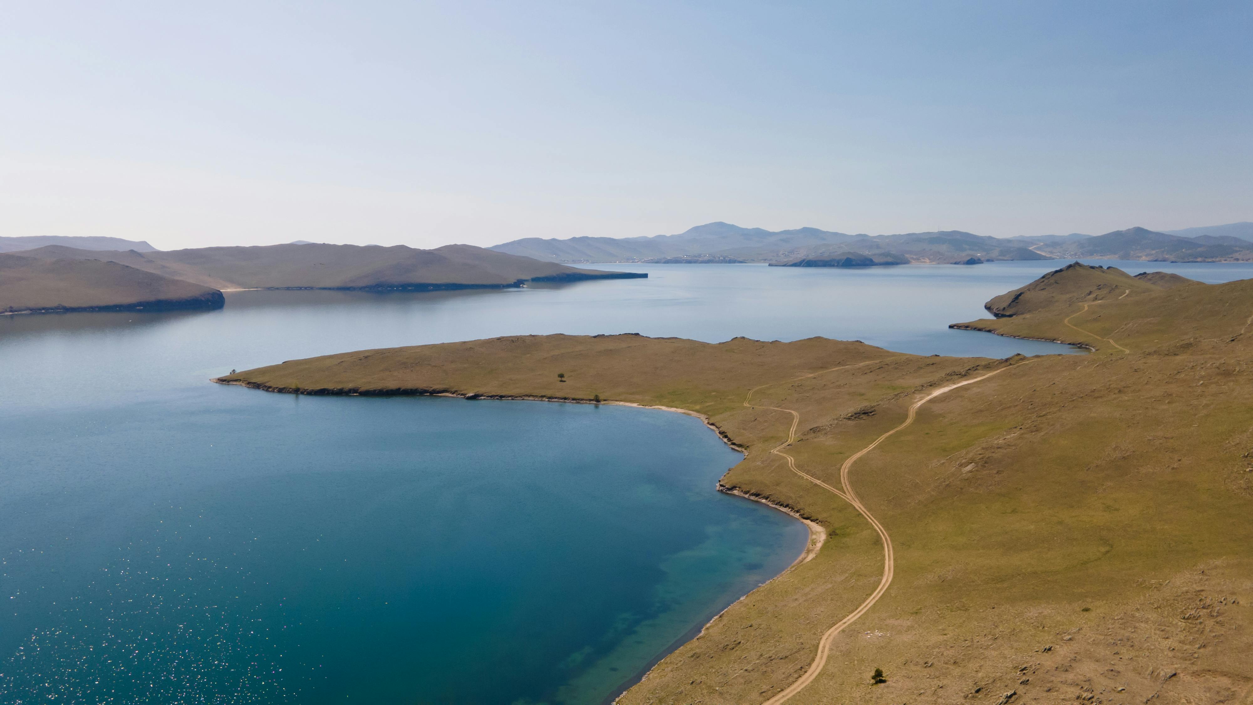A breathtaking aerial view of Lake Baikal in Russia showcasing its serene waters and rolling hills under a blue sky.