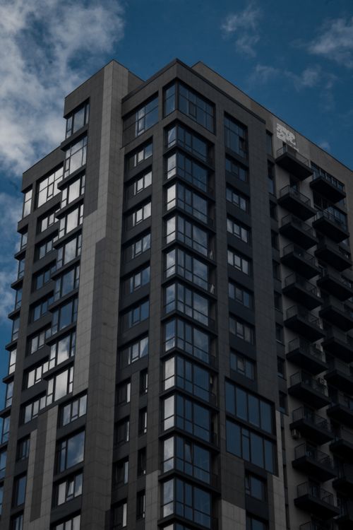 Free Low angle view of a modern skyscraper with glass windows against a partly cloudy sky. Stock Photo