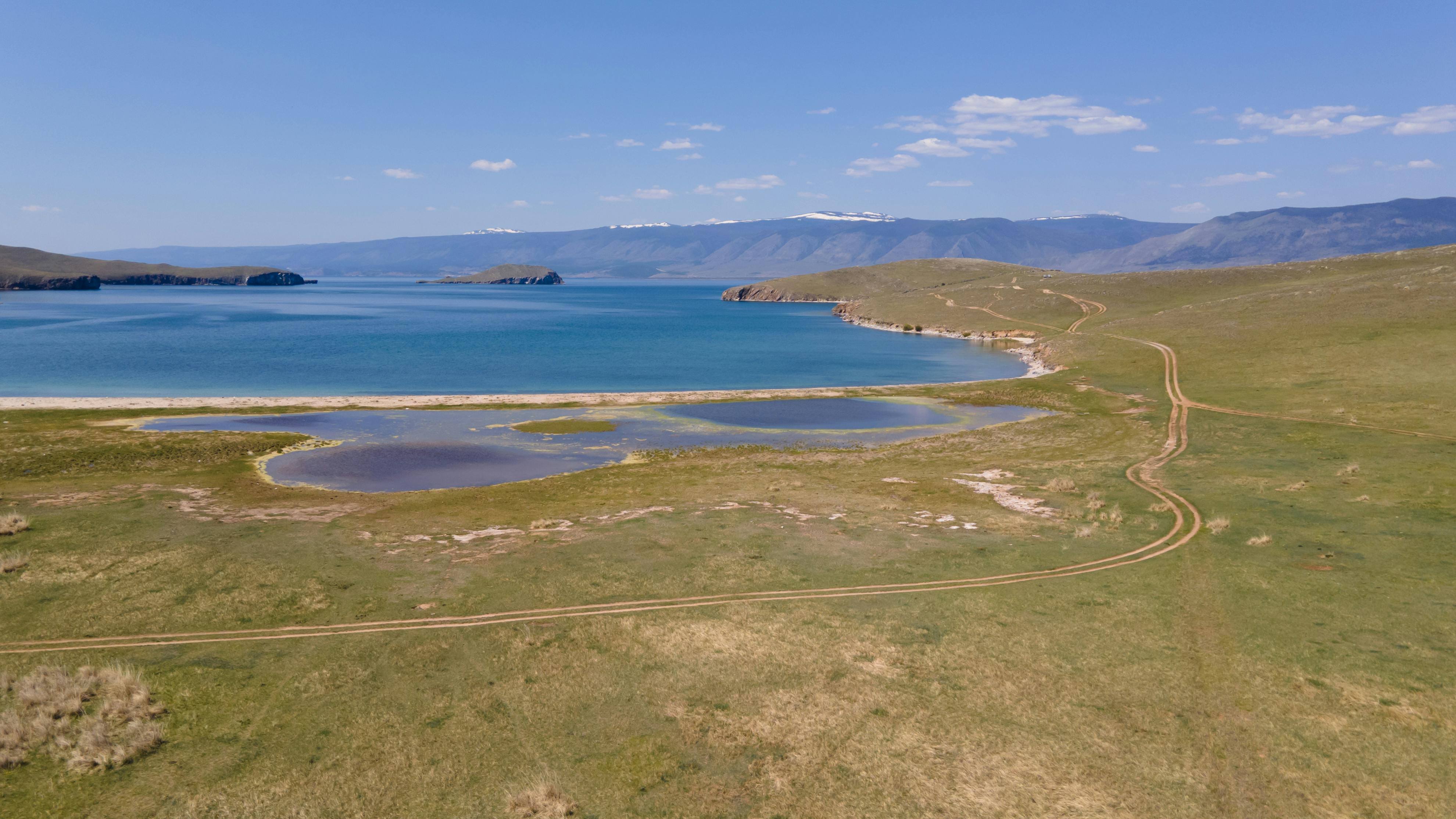 Scenic aerial view of Lake Baikal with grassy fields and blue waters under a clear sky in Siberia, Russia.