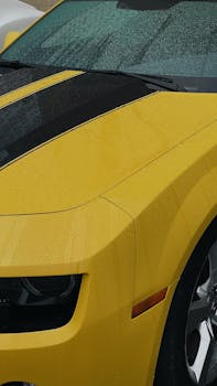 Close-up of a parked yellow Chevrolet Camaro with water droplets on the hood, captured outdoors.