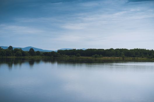 Calm waters reflect the sky and a tree-lined shore under a clear blue sky.