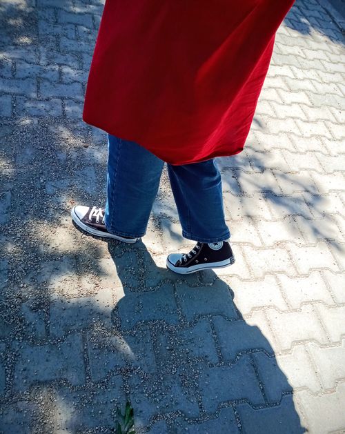 Free A person in denim pants and sneakers walking on a sunny paved path, creating a shadow effect. Stock Photo
