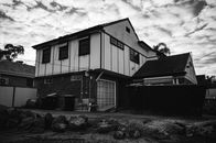 Grayscale Photo of House Under Cloudy Sky