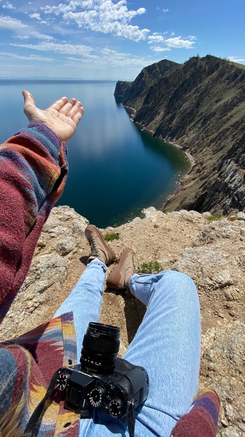 Free A serene view from a cliff overlooking Lake Baikal with a person seated, welcoming the vast landscape. Stock Photo