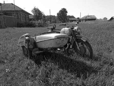 Classic vintage motorcycle with sidecar in a grassy rural setting, evoking nostalgia.