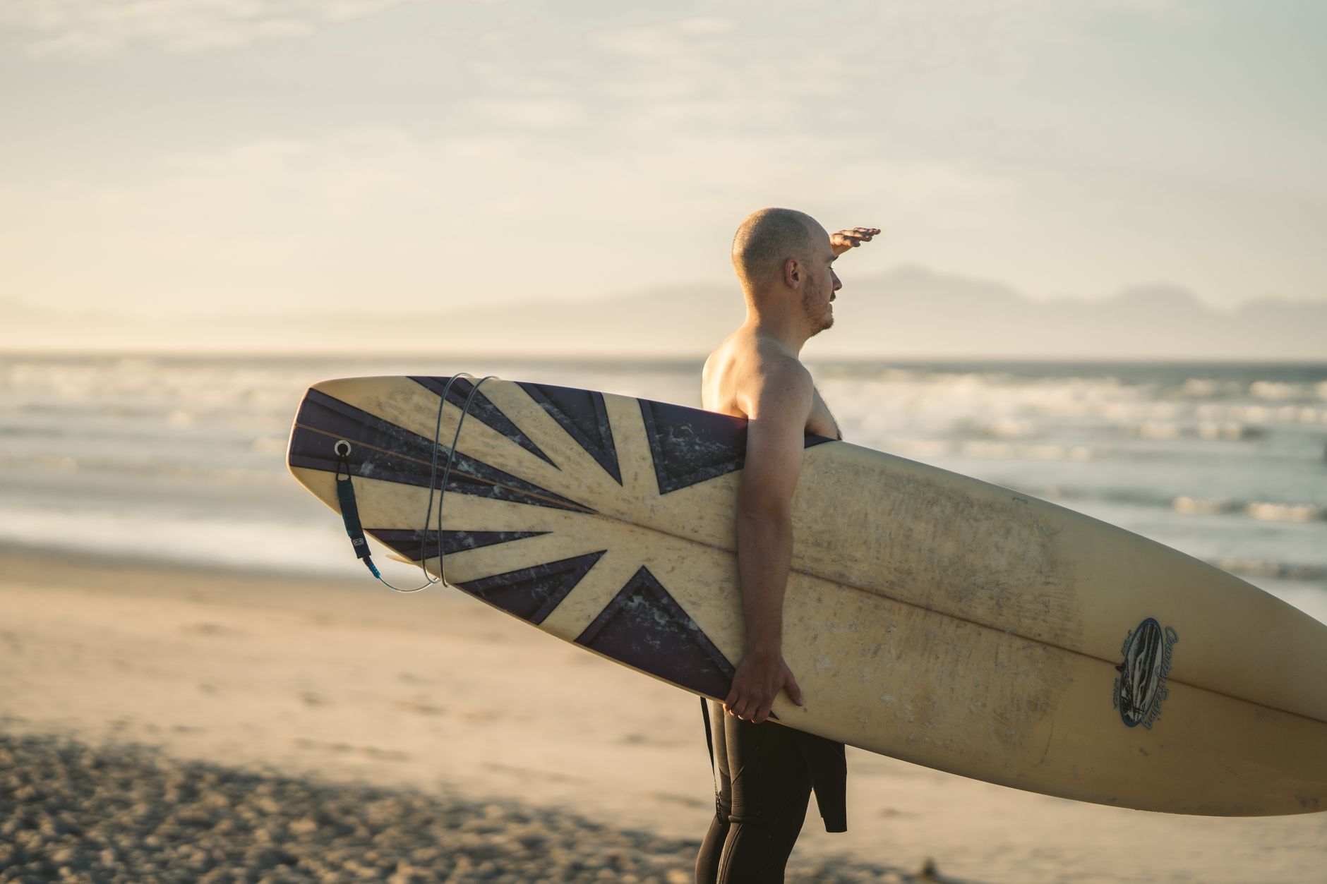 Surfer with a Union Jack surfboard looking out at the sea, Cornwall