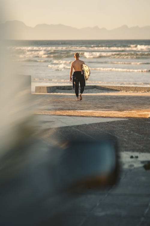 Back View of Man Carrying Surfboard while Walking towards the Beach