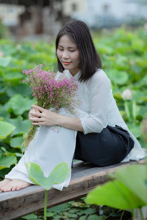 Woman Holding a Bunch of Flowers Sitting on a Wooden Deck