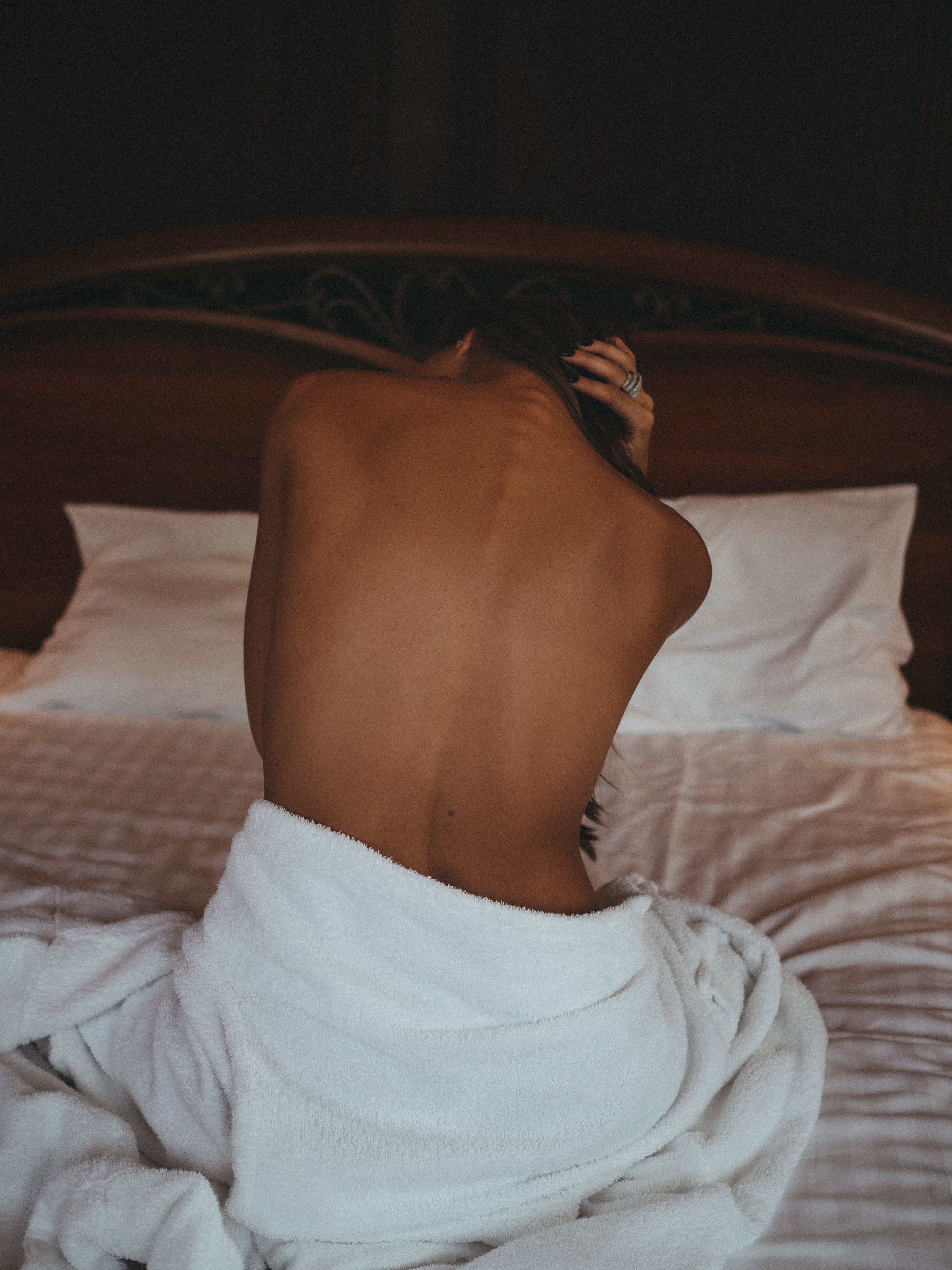 Back view of a woman wrapped in a blanket on a bed, exuding elegance and serenity.