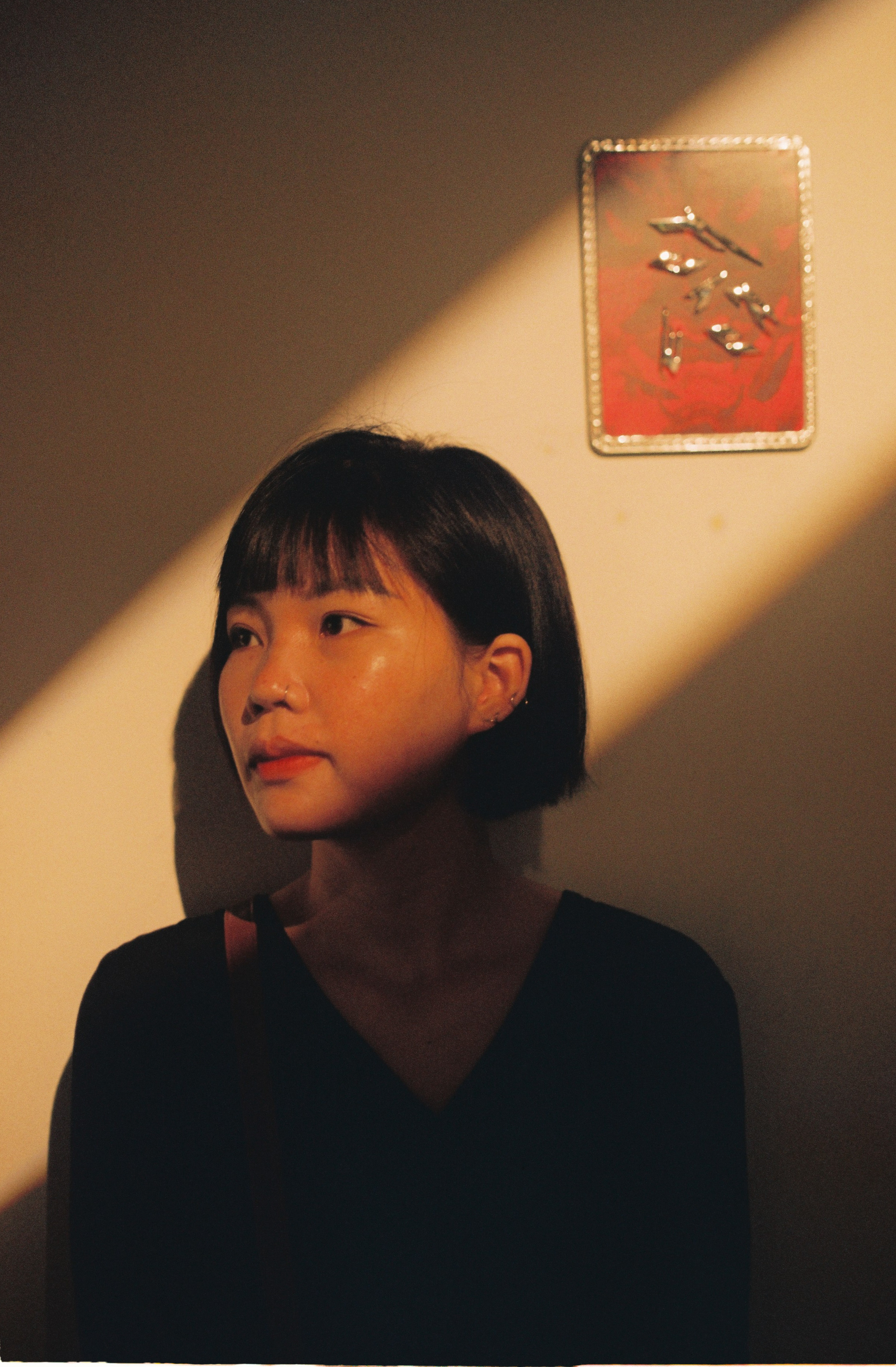 Asian woman in thoughtful pose with dramatic lighting creating strong shadows indoors.