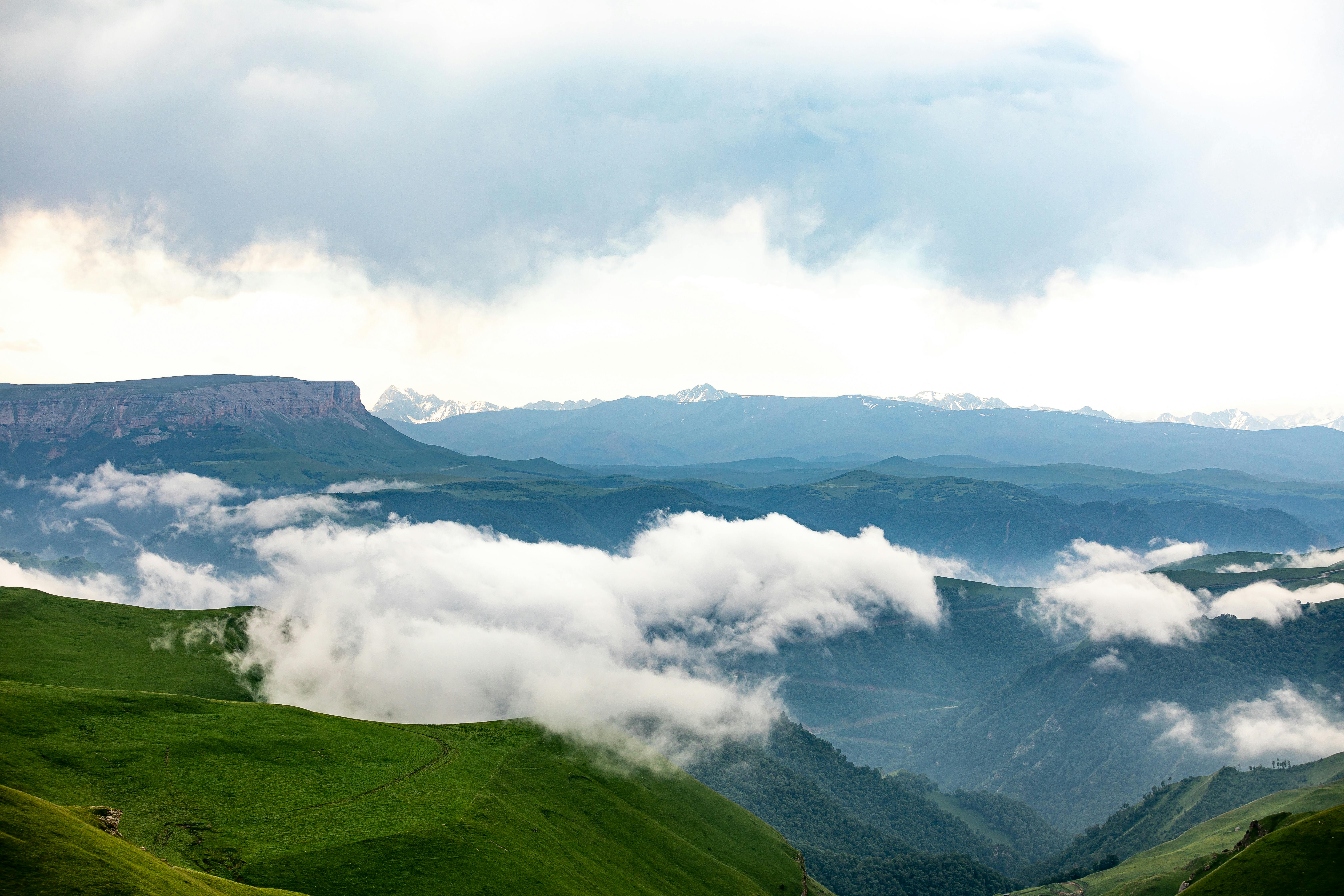 Free Breathtaking view of mountain ranges enveloped by lush greenery and rolling clouds. Stock Photo